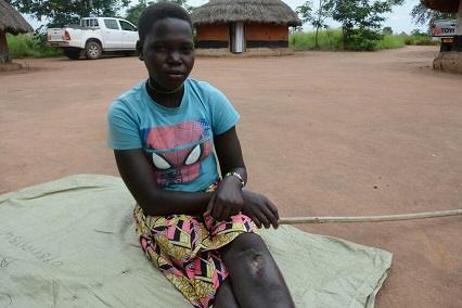 Teenage girl blue shirt sitting on ground outside in Uganda. 