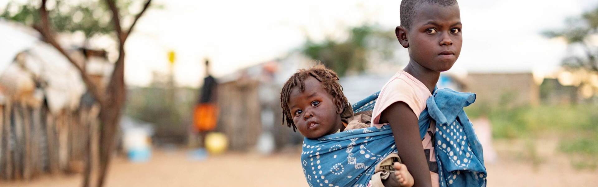 Mabel carries her brother Steven on her back in a colorful cloth shawl.