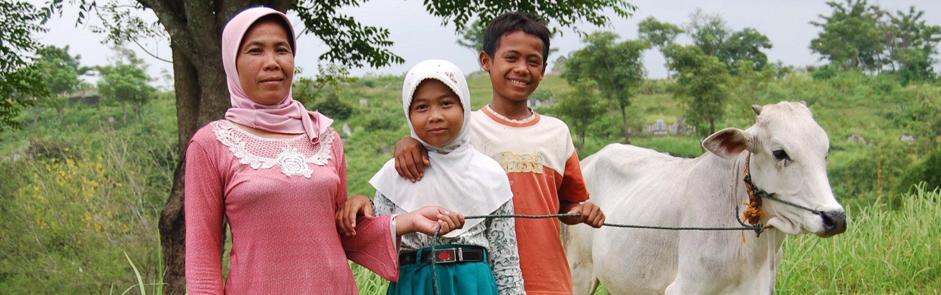 A family stands in a rural area holding a cow on a leash.