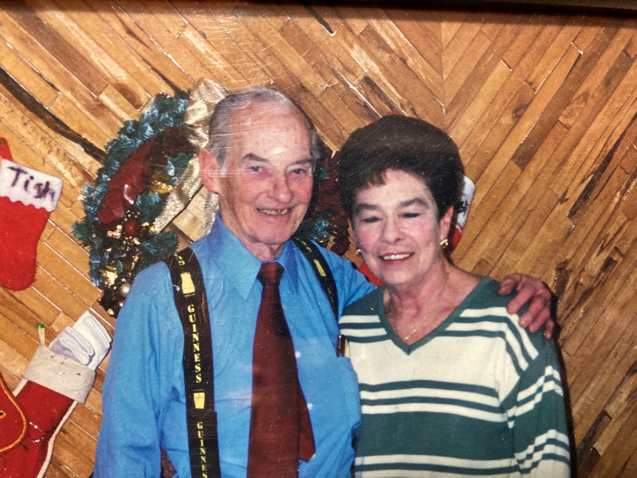 Man and woman stand in front of a mantle with Christmas stockings, smiling at the camera.