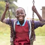 A little girl smiles while swinging on a swing in Uganda.