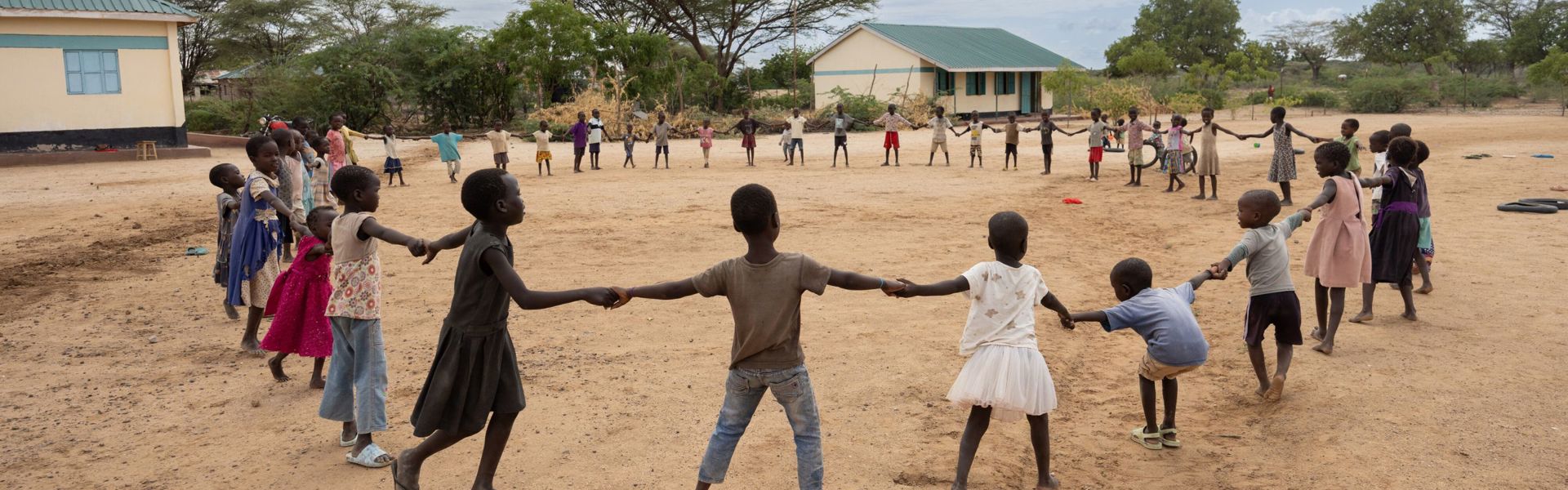 A group of children hold hands in a circle outdoors in Turkana County, Kenya