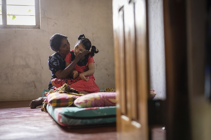 A mom holds her disabled daughter on a mattress in the middle of a room in Sri Lanka.
