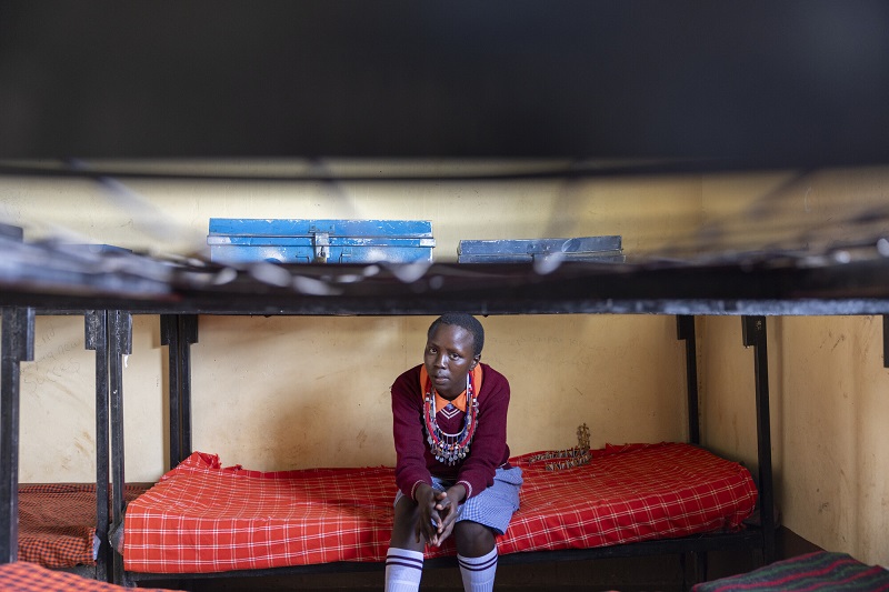A teenage girl in Kenya sits on a dormitory bed.