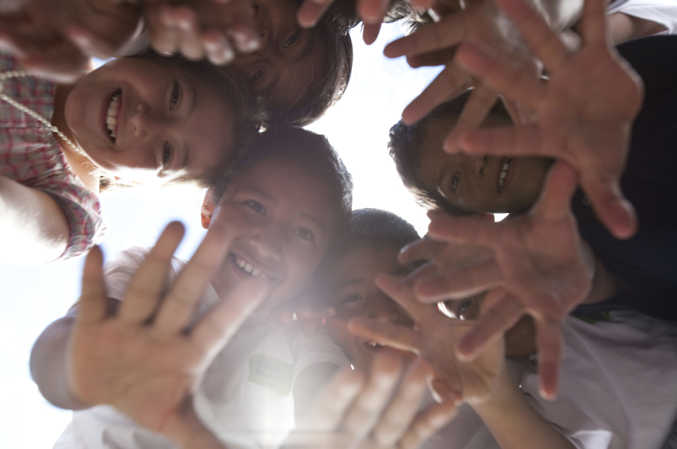 A group of children in Ecuador, gathered in a circle above the camera, smiles and waves.