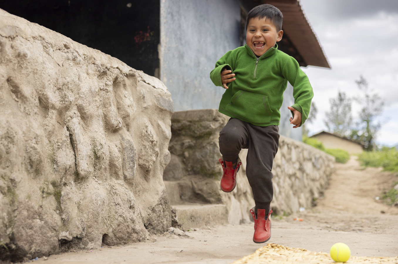 A preschool-age boy runs down a street in Ecuador, laughing.