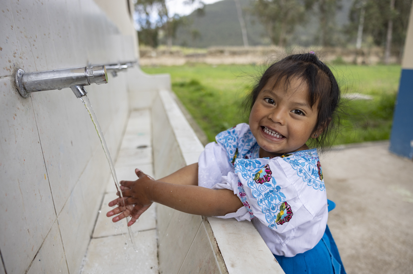 A young girl in Ecuador washes her hands, smiling at the camera.