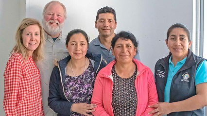 A group of adults stands indoors in Ecuador, smiling.