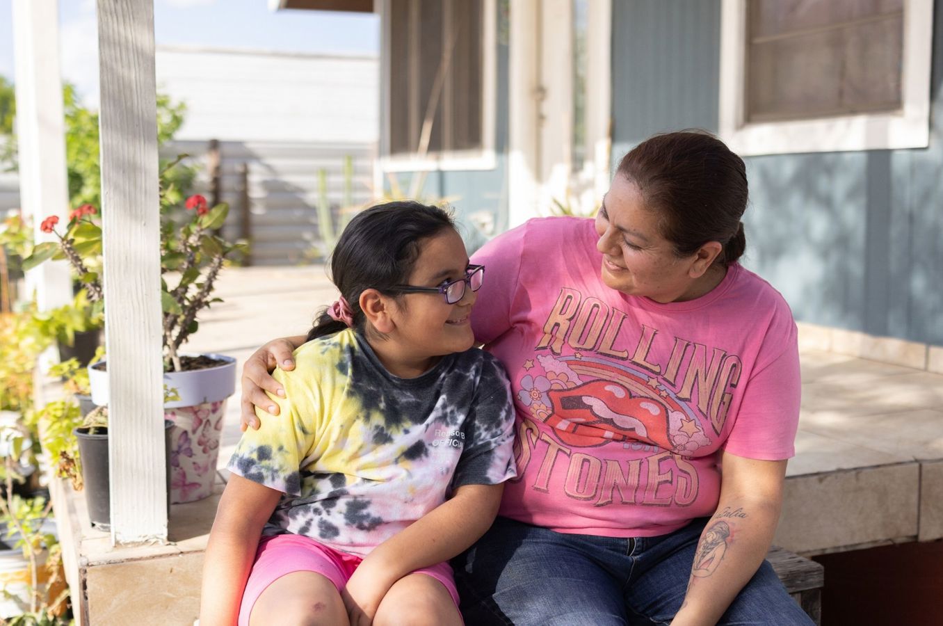 A mom and her daughter sit on a porch in Rio Grande Valley, Texas, hugging.