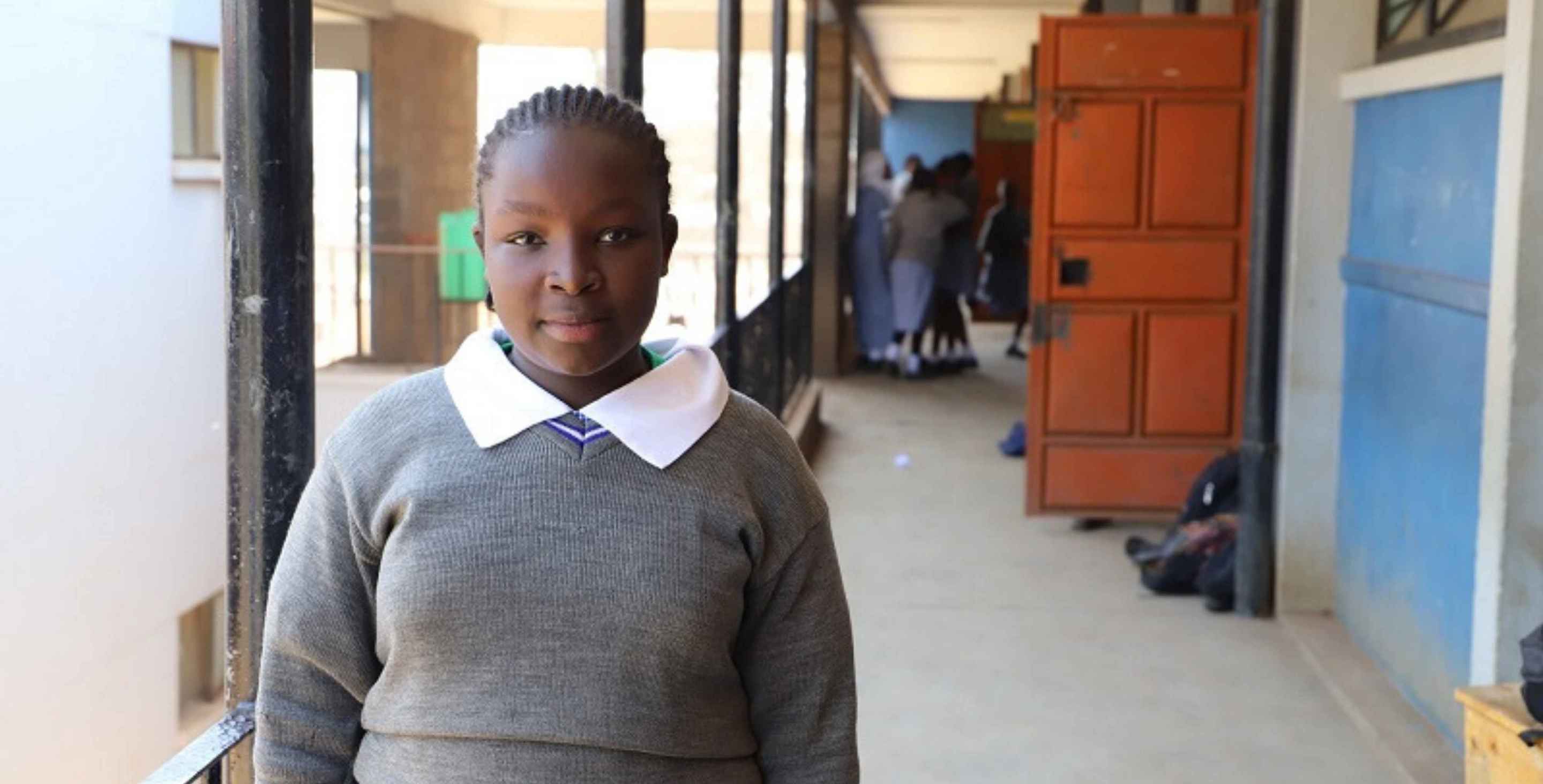 Ruth, wearing a school uniform, stands outside her school