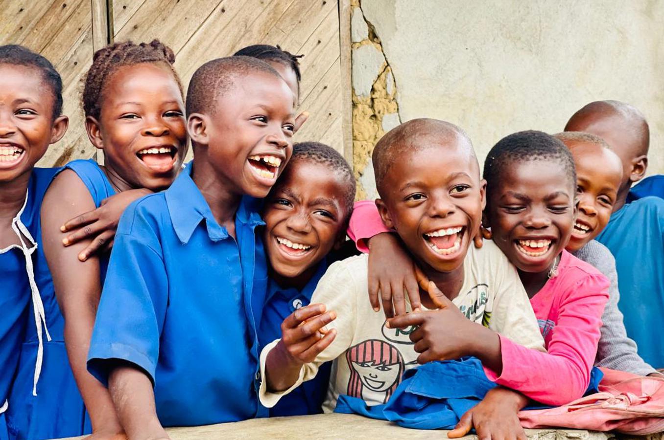 Children in Sierra Leone gather in a group, laughing toward the camera.