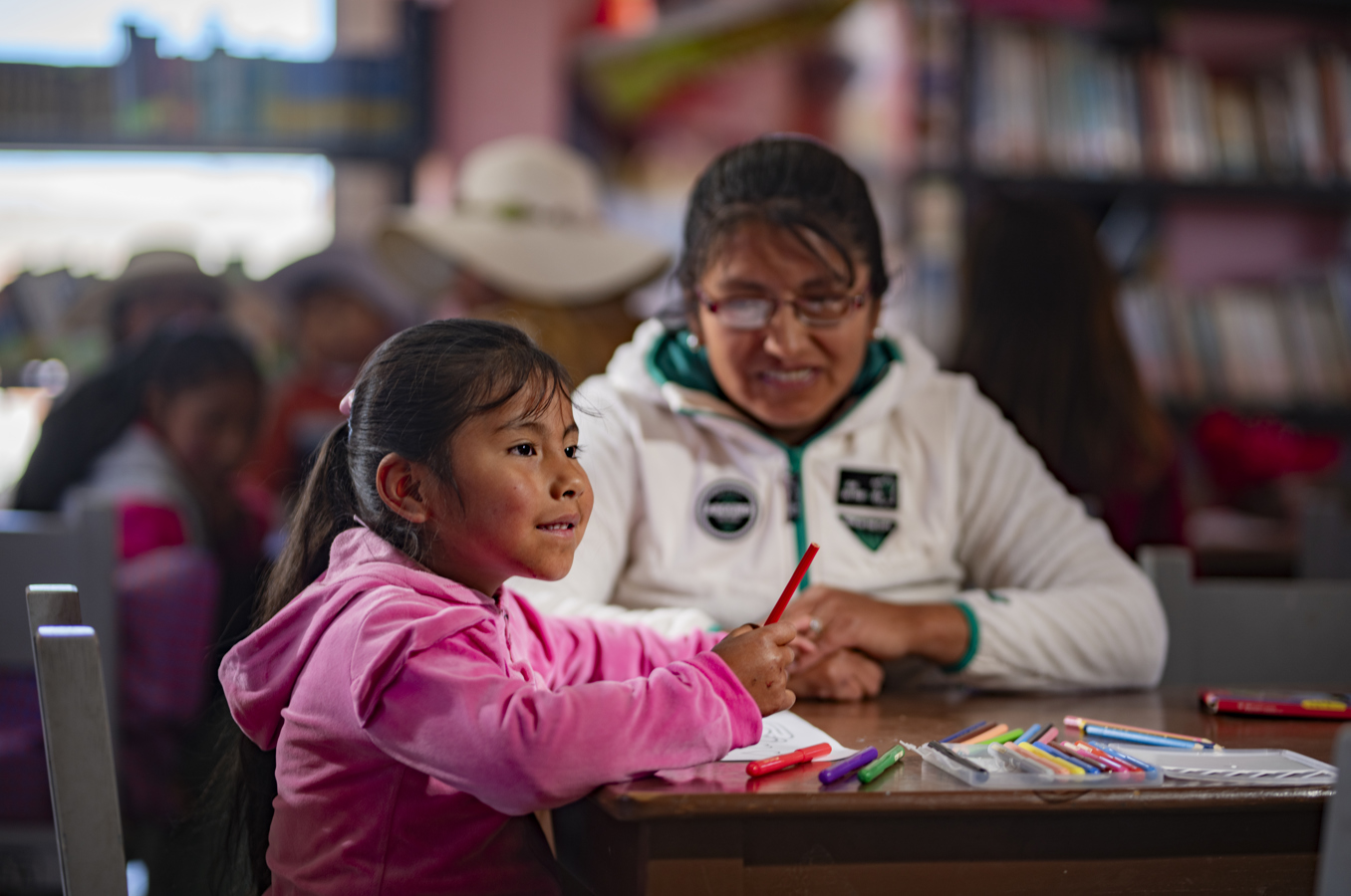 A child sits at a desk in Bolivia with a staff member of ChildFund's local partner.