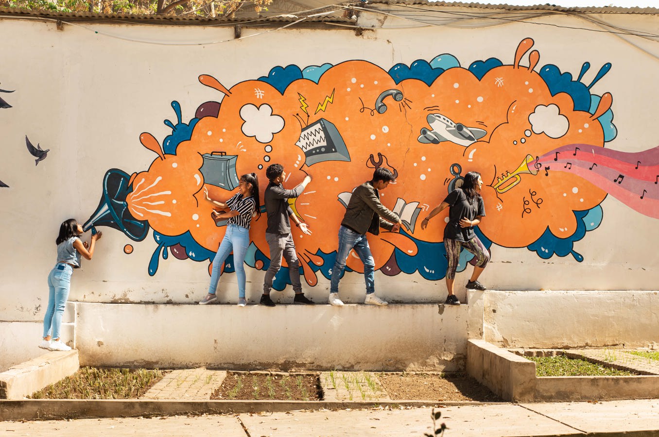 A group of youth pose in front of a mural in Bolivia that features paintings of loudspeakers.