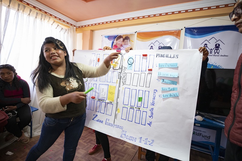 A young woman in Bolivia gestures to a map of her community, smiling.
