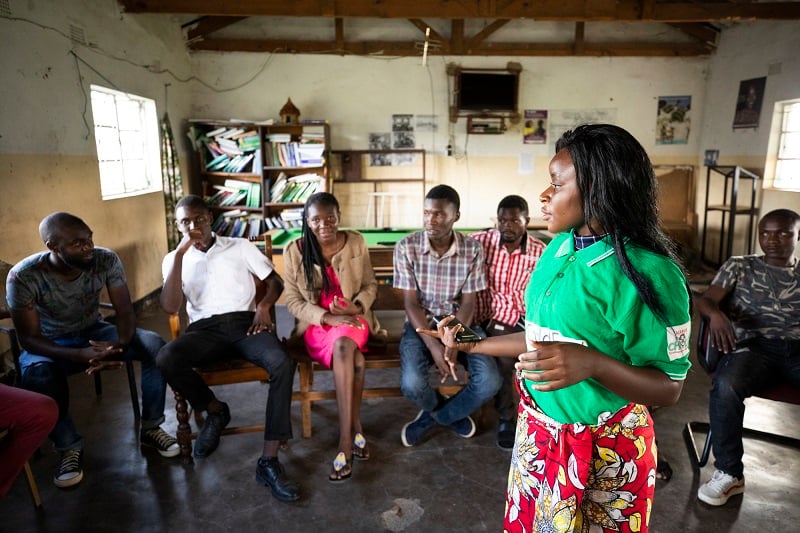 A young woman in Zambia talks to a group of youth in a community center.