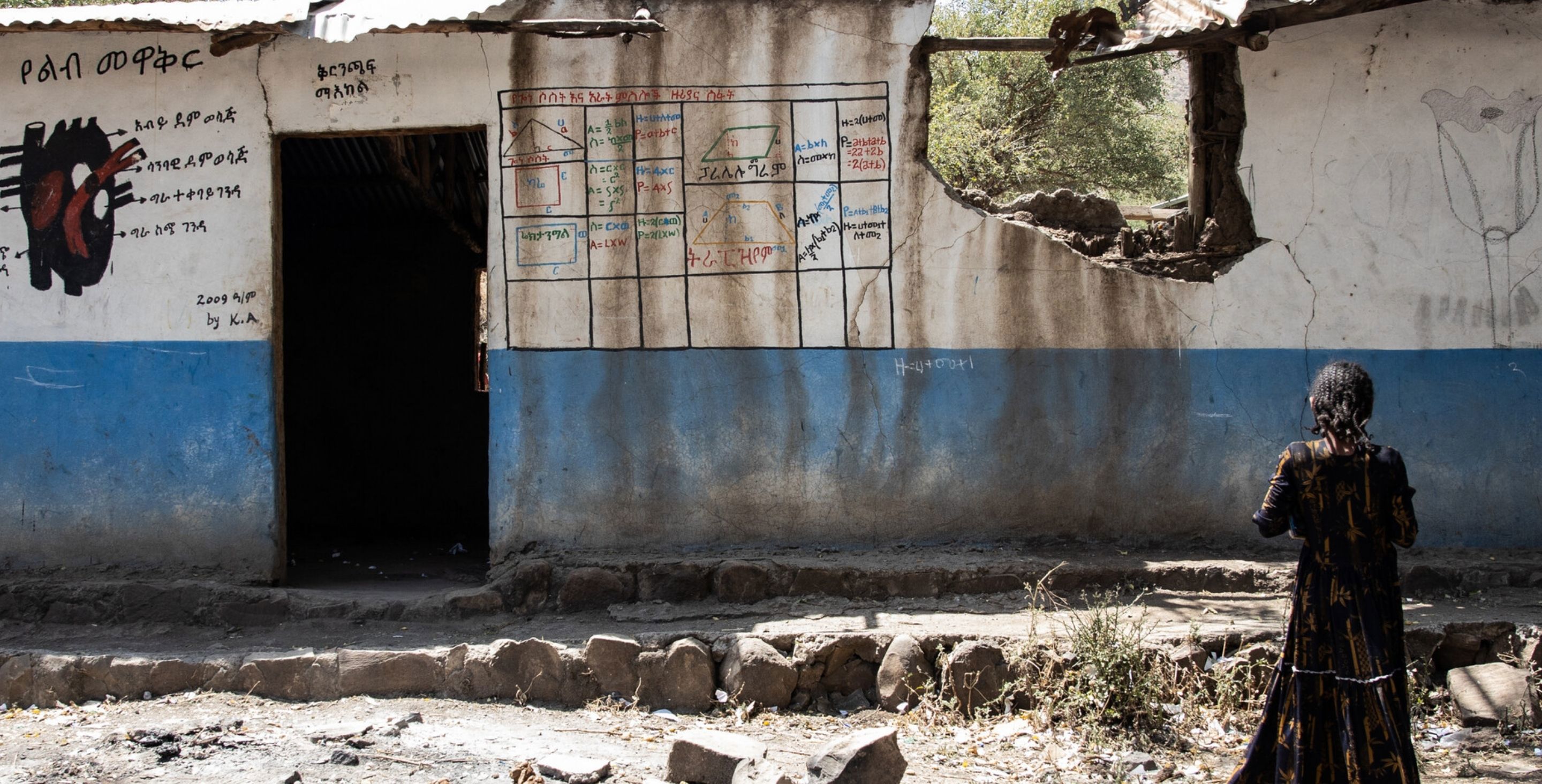 A girl in Ethiopia stands facing a former school building that has been destroyed in a war, her back to the camera.
