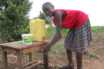 A girl in Uganda washes her hands outside from a yellow jerrycan.