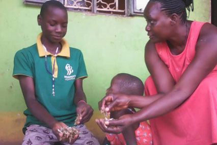 A family in Uganda sits outside holding fish, preparing food.