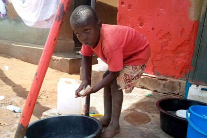 A boy washes his hands in a bucket outside in Uganda.