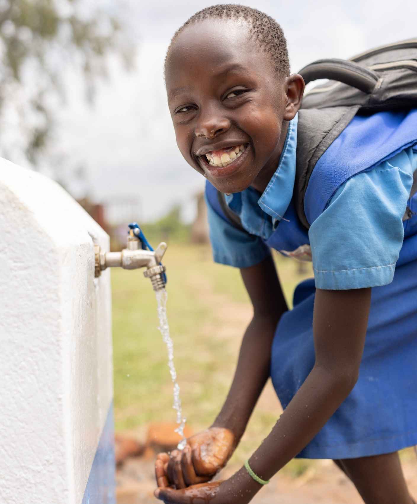 A young girl pours water over her hands from a spout.