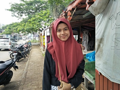 Young woman in Indonesia stands looking at camera smiling.