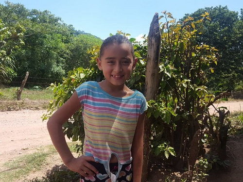 Girl in Honduras stands looking at camera smiling.