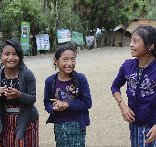 Girl in Guatemala stands with two friends smiling.