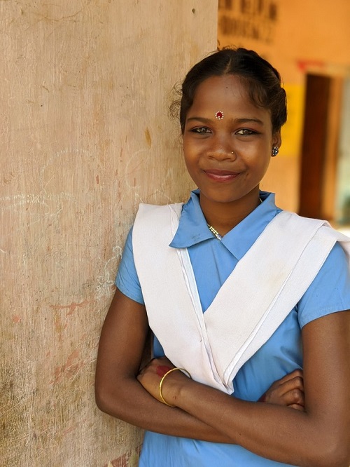 Young woman in India stands looking at camera smiling.