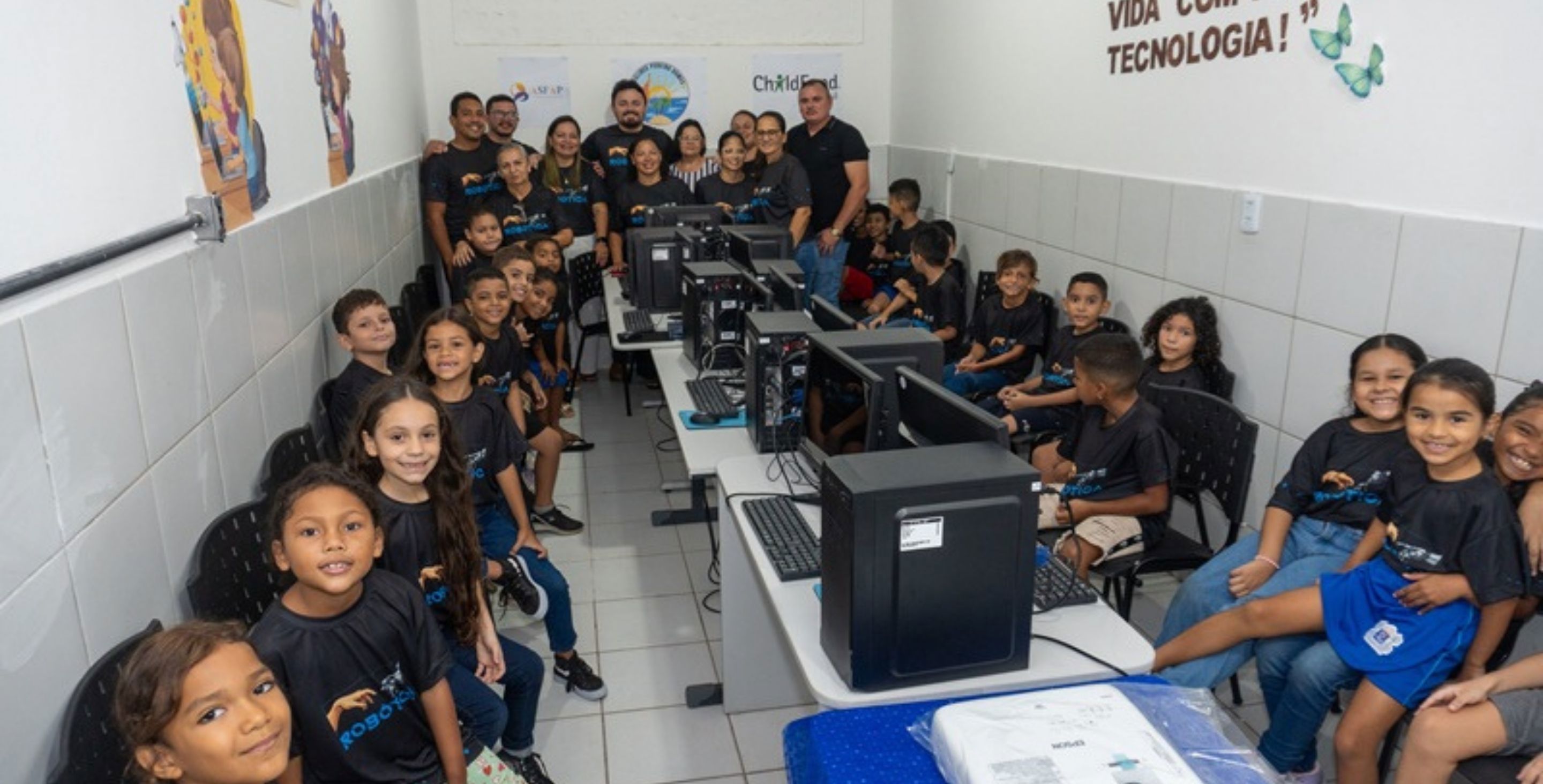 A group of children sit at computers at a computer lab in Brazil, with their teachers in the background.