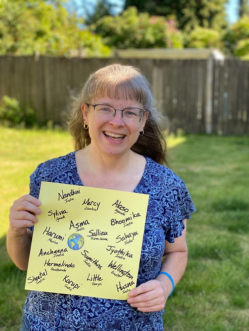 A woman, smiling at the camera, holds up a piece of paper with all 18 of her sponsored children's names.