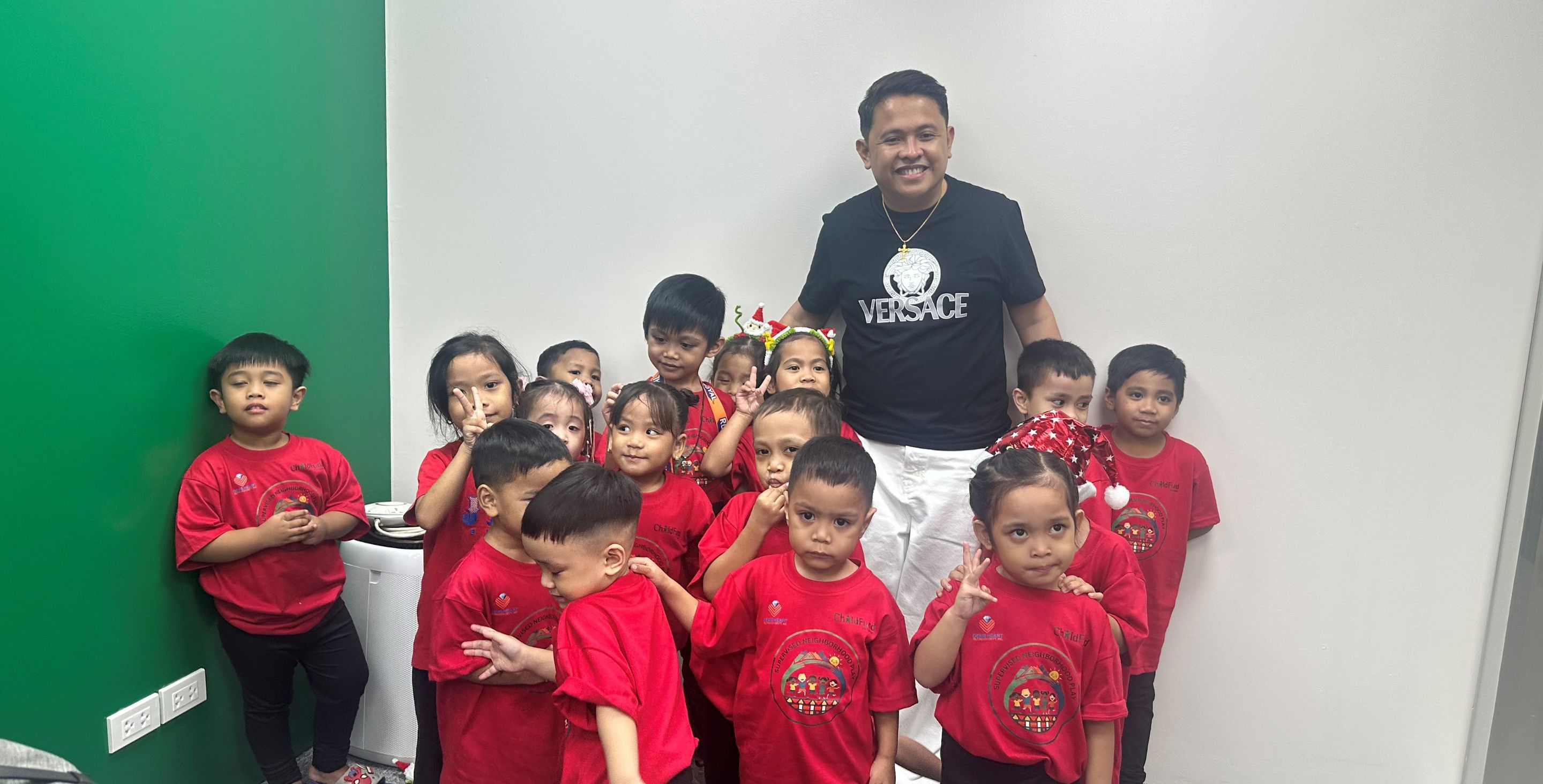 A man in the Philippines stands in a room with a group of small children, smiling.