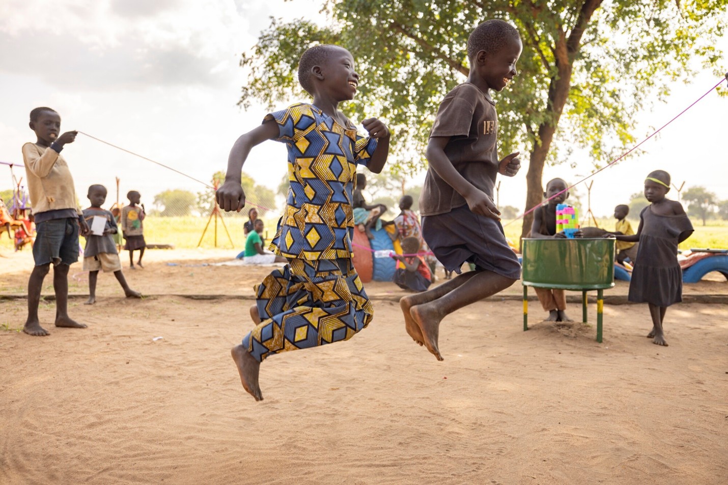 A group of children play jump rope in a rural setting.