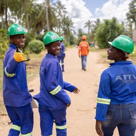 A group of young people in Mozambique walk down a dirt road, wearing blue uniforms and green hard hats.