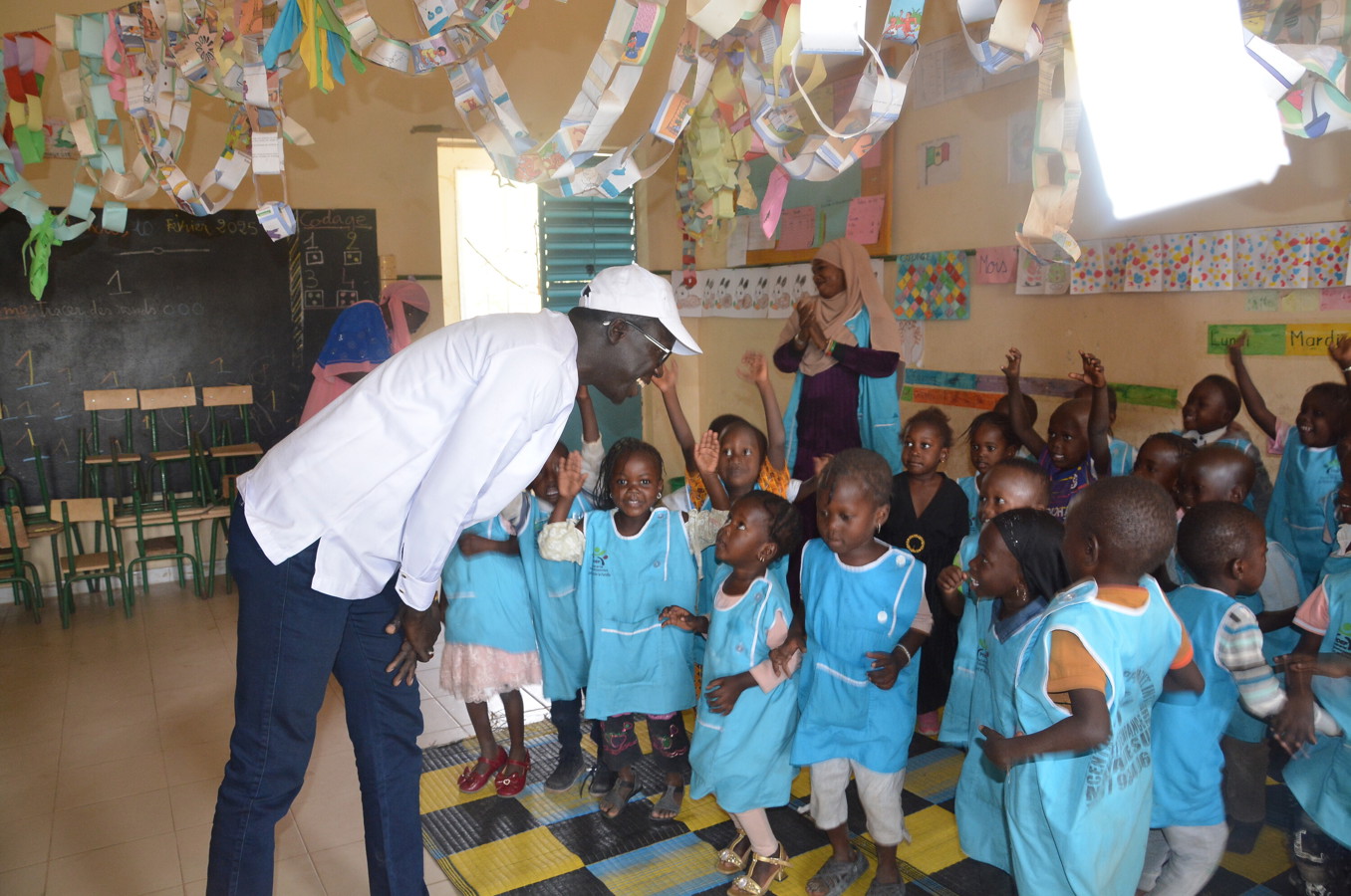 A man stands over a group of small children at an ECD center in Senegal, smiling.