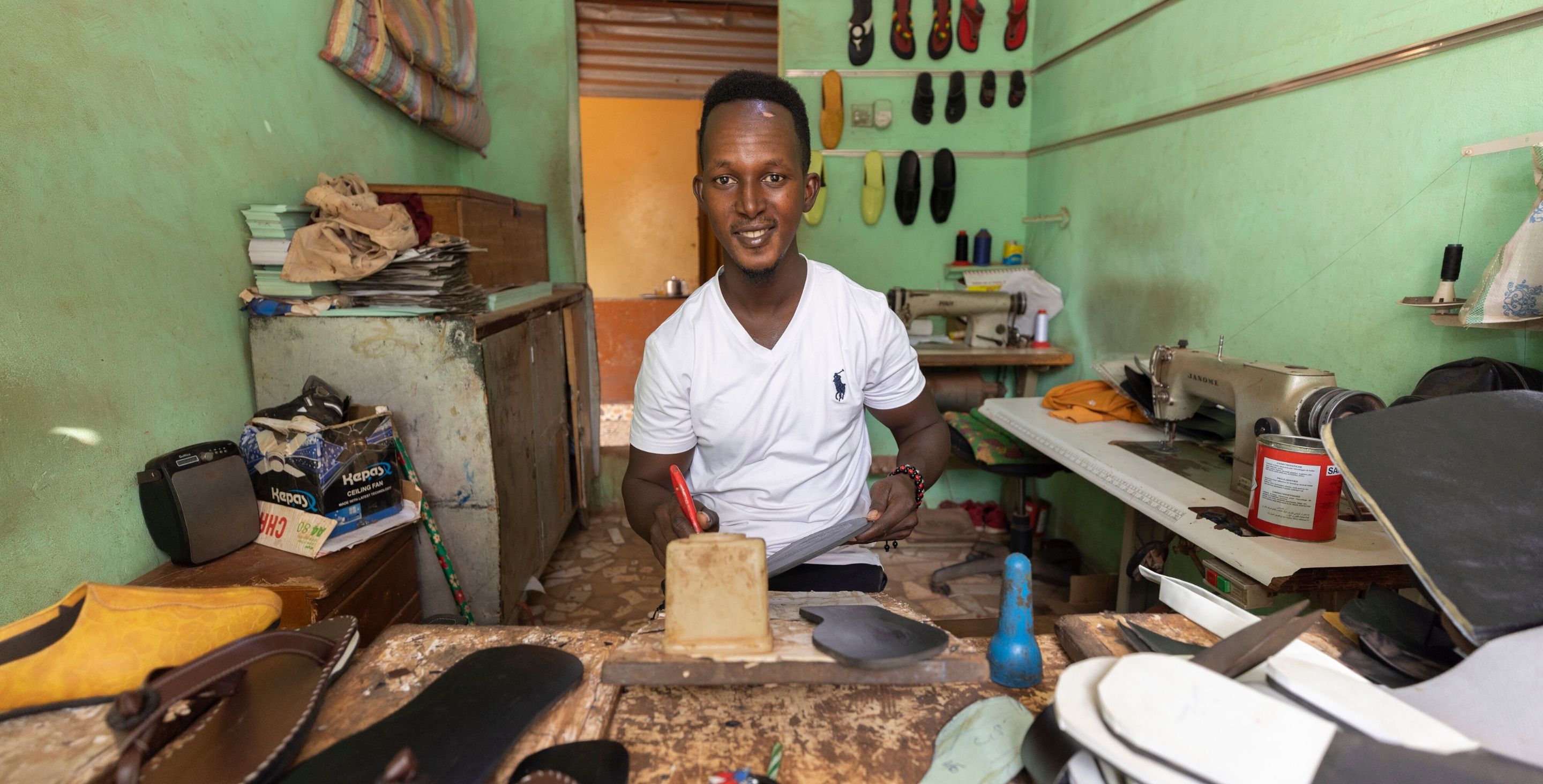 A young man in The Gambia sits in a room making shoes.