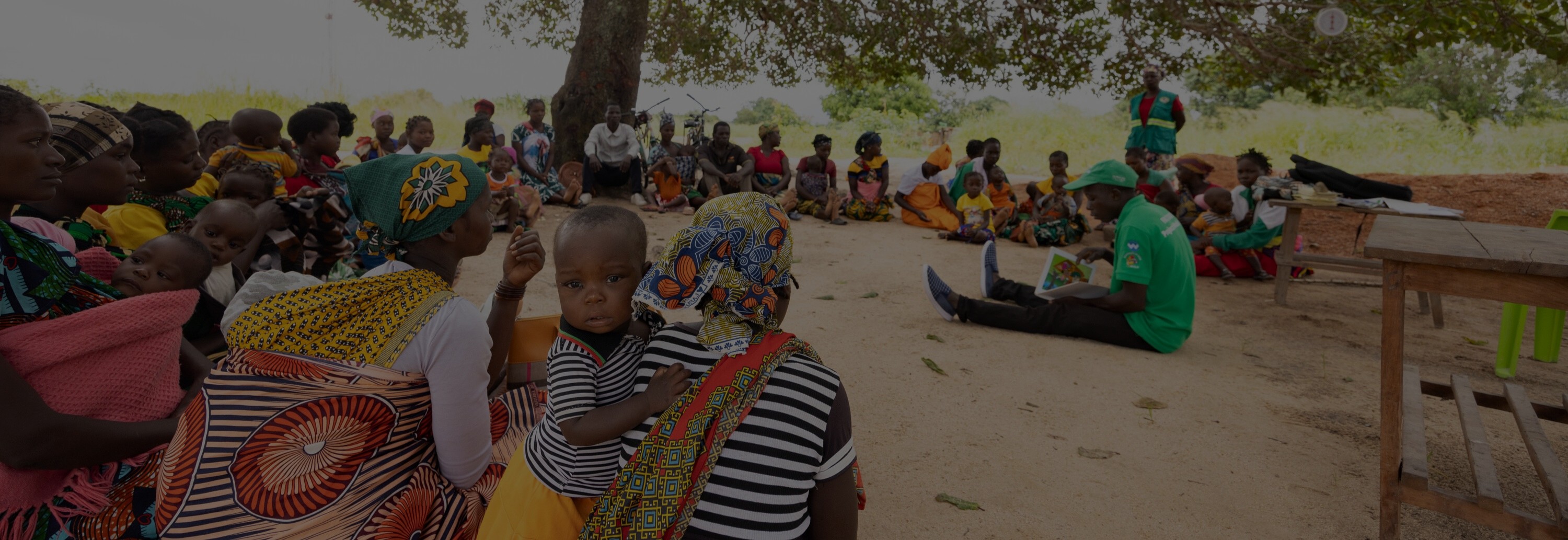 A group of children and parents sit under a tree.