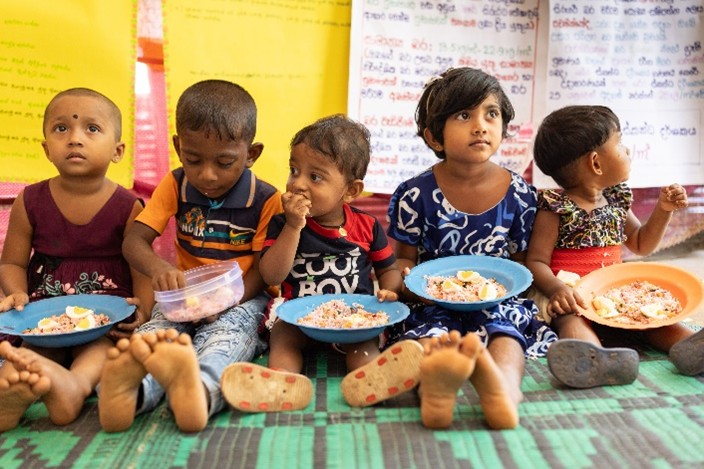 A group of children in a classroom eat a meal.