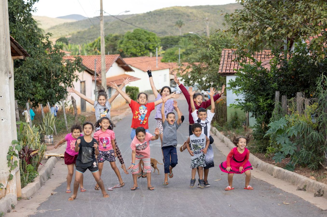 A group of children jump for joy in the middle of a road, waving colorful flags.