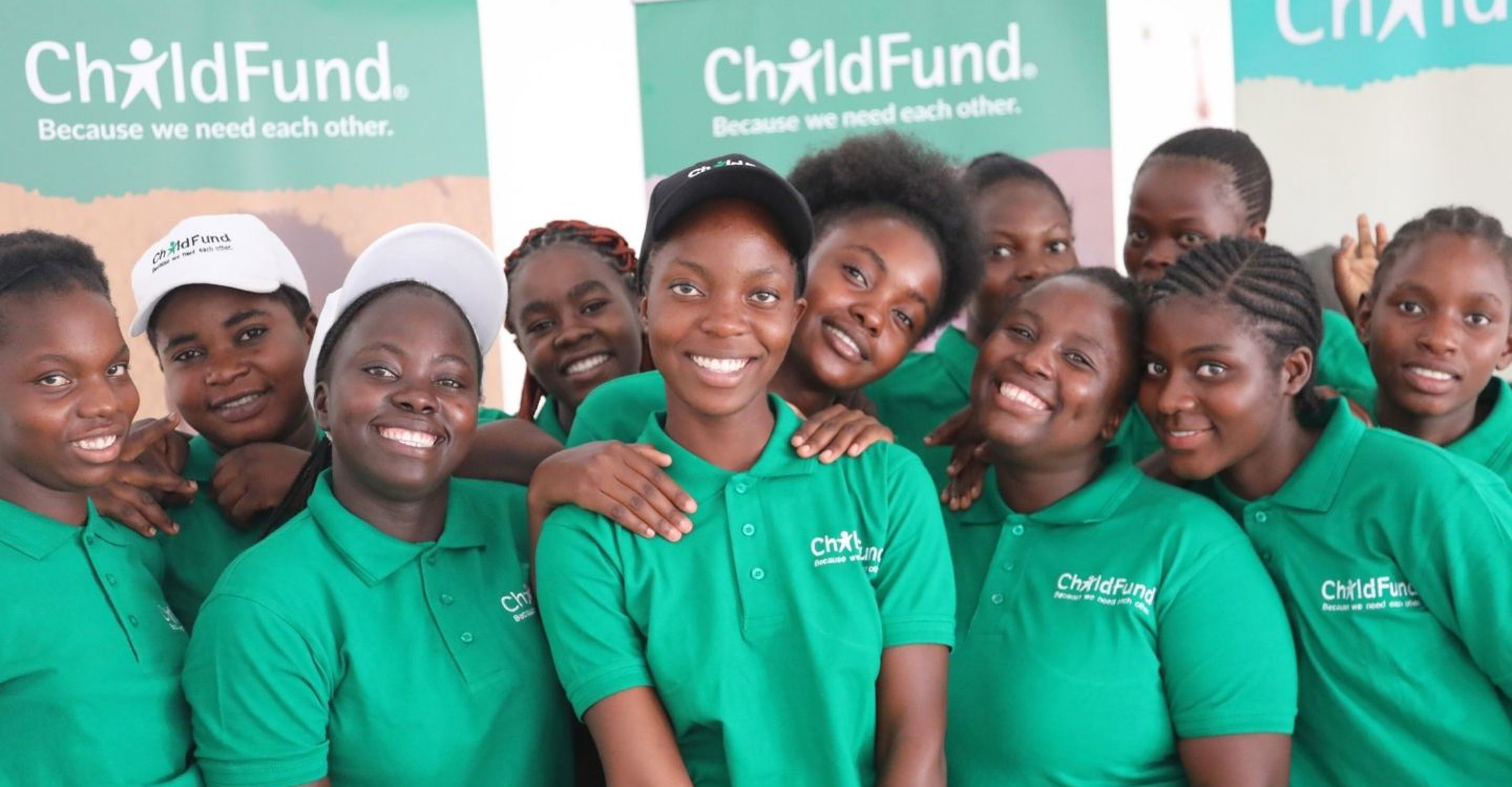 A group of youth in Zambia stand together, wearing ChildFund shirts and smiling