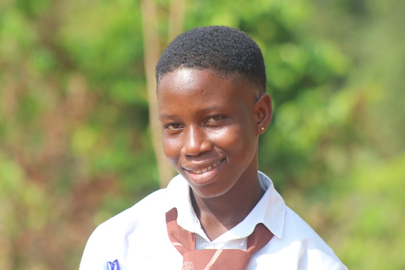 A teenage girl in Sierra Leone smiles at the camera, wearing her school uniform.