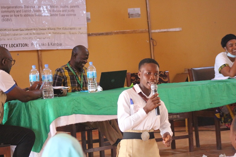 A teenage girl in Sierra Leone speaks with a microphone in front of a group of adults.