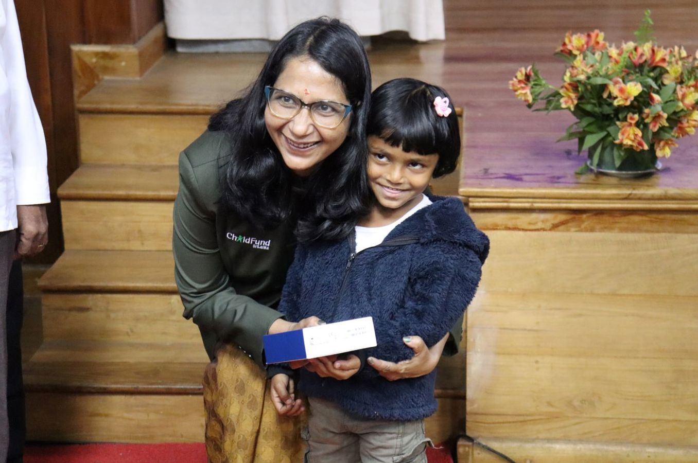 A woman with a bhindi on her forehead hugs a little girl as both smile.
