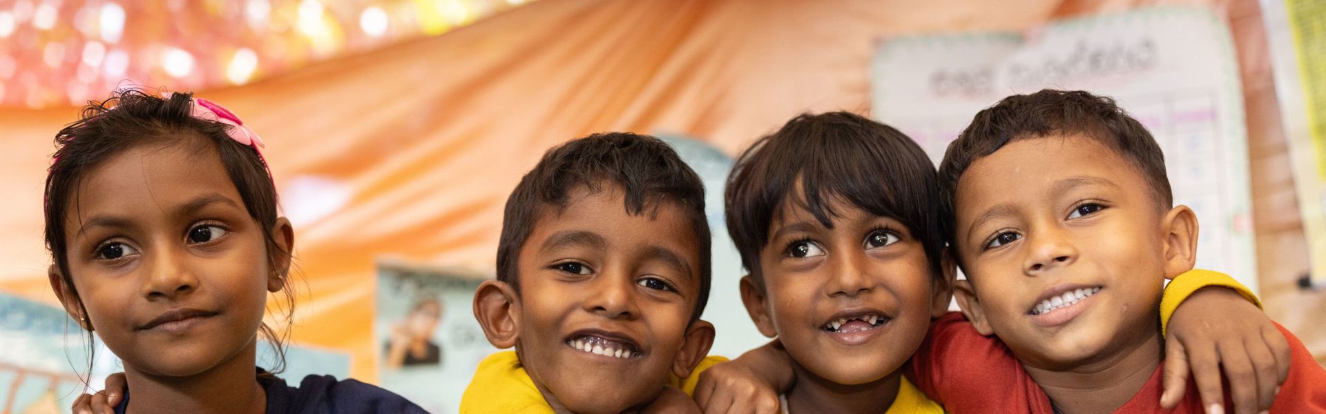 A group of children in Sri Lanka sit together, smiling at the camera.