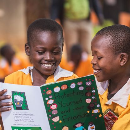 Two little boys in Uganda sit on the ground reading a book called 
