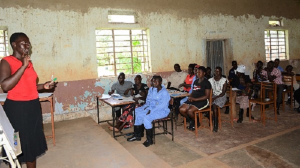 Teacher teaches a class of mostly young women in a building in Uganda.
