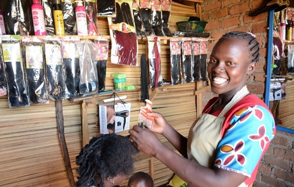 Girl does hair in a salon in Uganda, smiling at the camera.