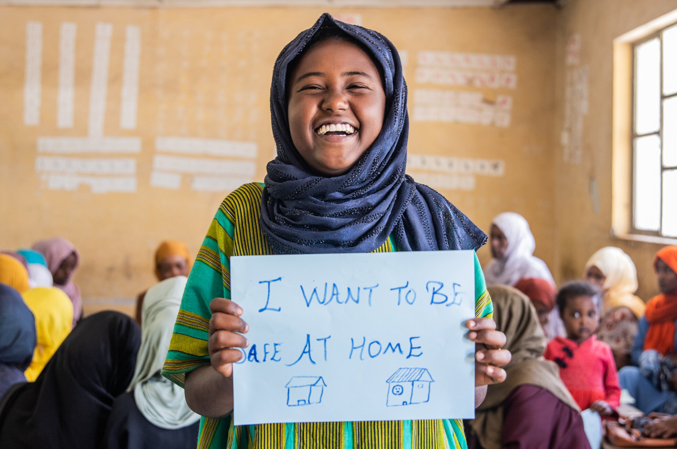 A teenage girl in Ethiopia holds a sign she made, smiling.