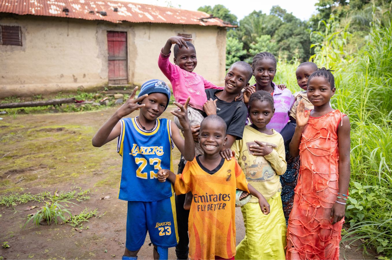 Children in Guinea smile together standing in front of a hut.
