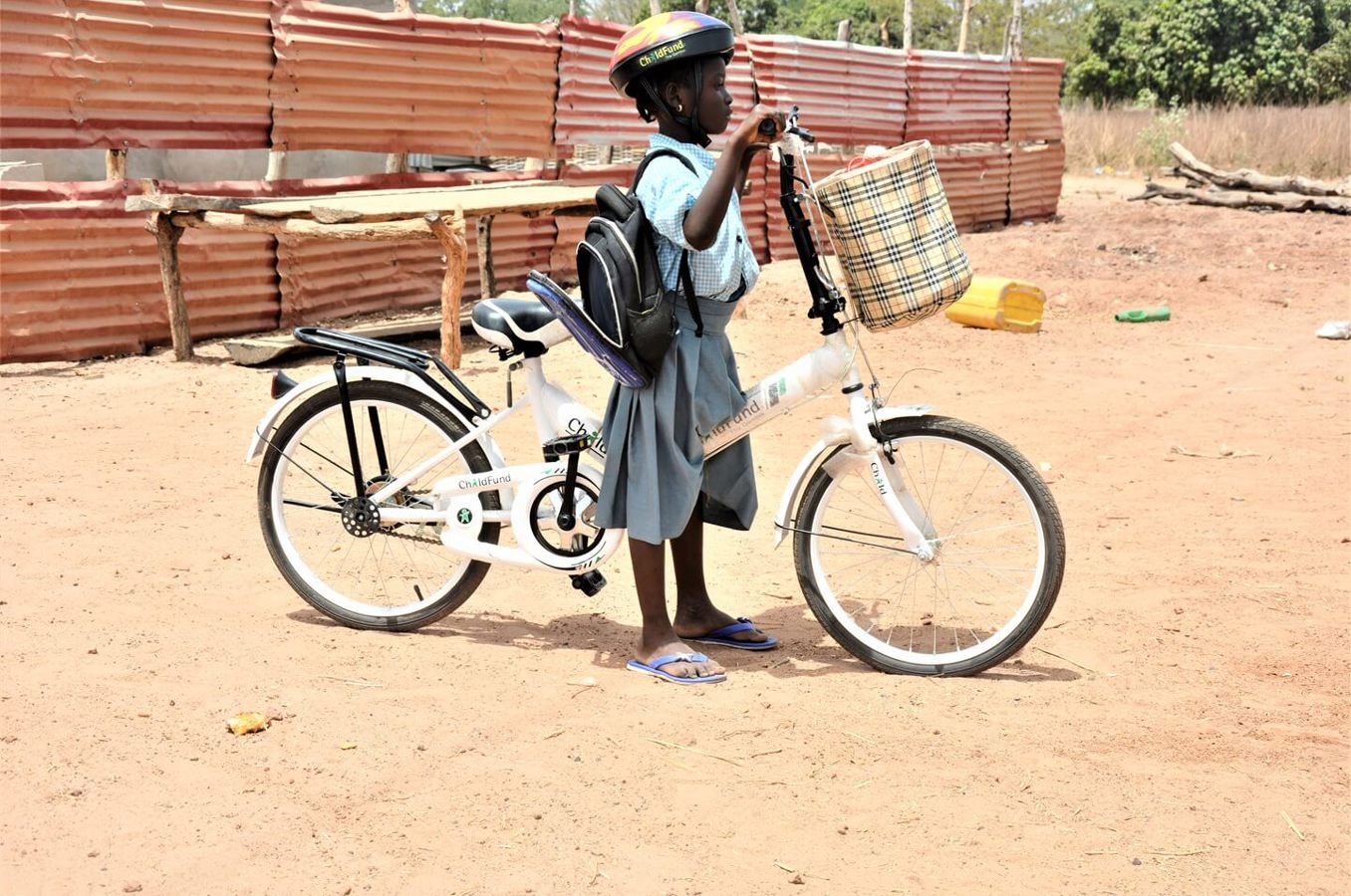A girl in The Gambia wearing a ChildFund helmet rides a white ChildFund bike.