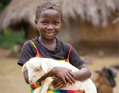 Young girl in rainbow dress smiles while holding baby goat